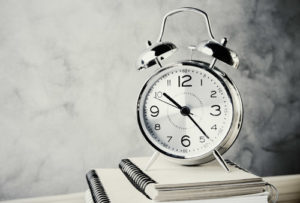 Front view of alarm clock and copybooks on concrete background