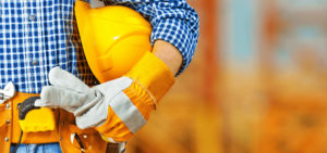 Close-up of construction worker's hand in a work glove, with a hard hat under his arm