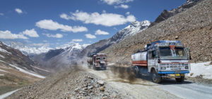 Two gravel trucks traveling up a mountain road with other mountains in the background