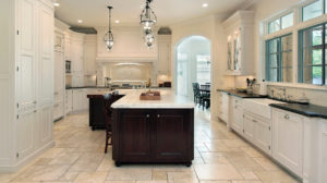 Large, white home kitchen with chandelier lighting and dark brown accents