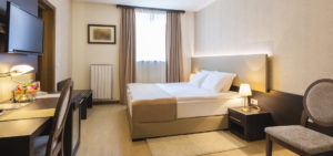 Image of a clean hotel room with beige paint and linens as well as dark wood furniture