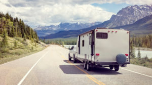 Pickup truck pulling an RV down a paved road with mountainous terrain on either side